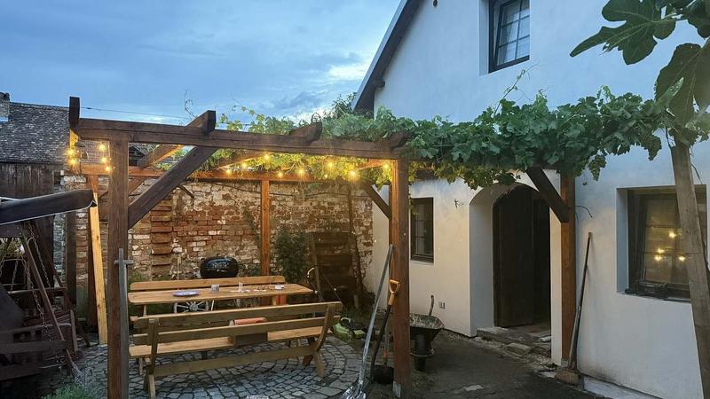 Pergola se světýlky a dřevěným posezením před sklípkem
