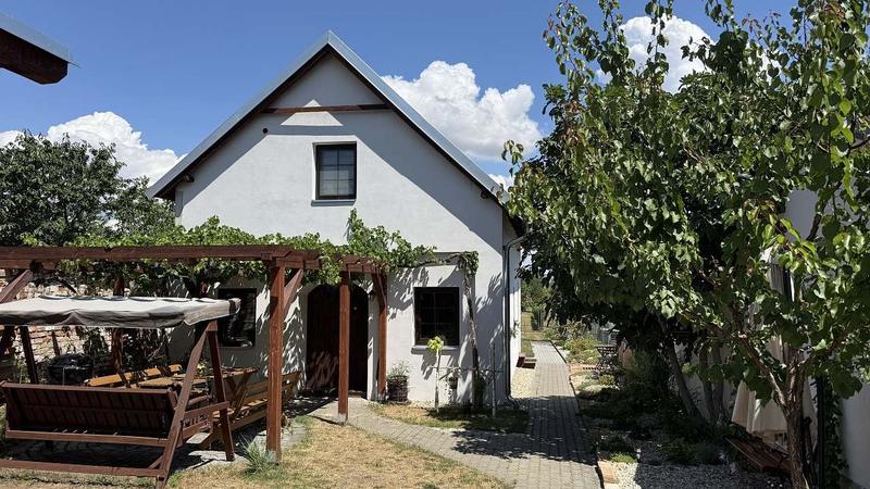 Bílý domek s pergolou obrostlou révou, houpačkou s lavicí a dlážděnou cestou v Drnholci